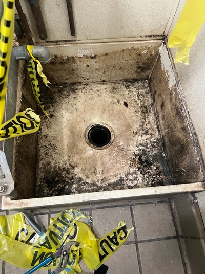 Mop sink with visible gaps around drain and wall joints causing water leakage.