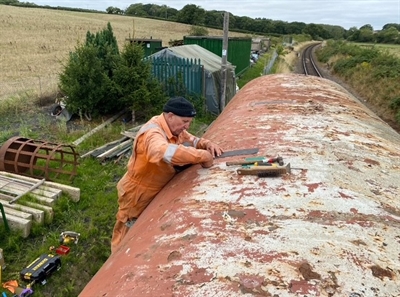 A man cleans the roof of the train carriage, preparing the surface for application