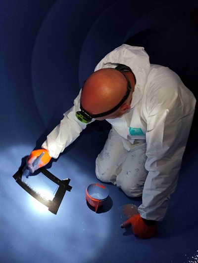 A man kneeling down inside a large tube, coating the surface of the tube