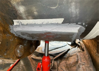 A plate held in place by a clamp now covers the defect hole in the pipe