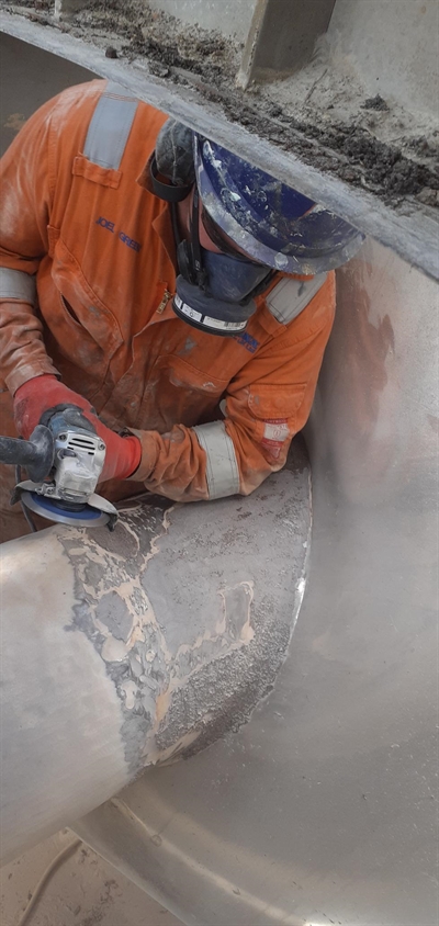 A Man with power tools and personal protection equipment working on eroded areas of screw conveyor