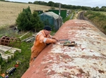 A man cleans the roof of the train carriage, preparing the surface for application