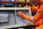 A man in overalls and PPE is applying the coating with a brush